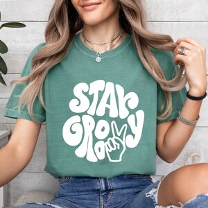 May include: A green t-shirt with a white graphic that says "Stay Groovy" with a peace sign.