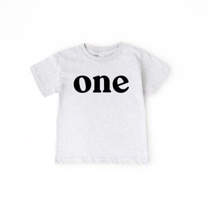 May include: A light gray toddler t-shirt with the word "one" printed in bold black letters across the front. The shirt has short sleeves and a crew neck.