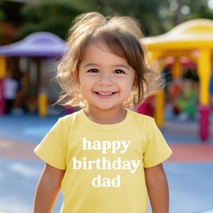 May include: A young child wearing a yellow t-shirt with the text "happy birthday dad" printed in white.