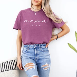 May include: A mauve t-shirt with the text "mama est 2025" in white script.