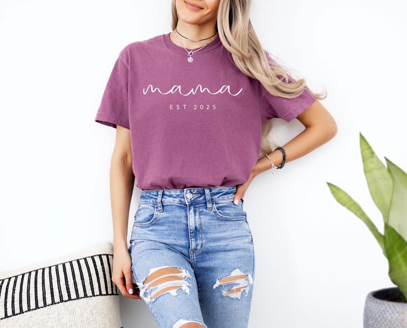 May include: A mauve t-shirt with the text "mama est 2025" in white script.