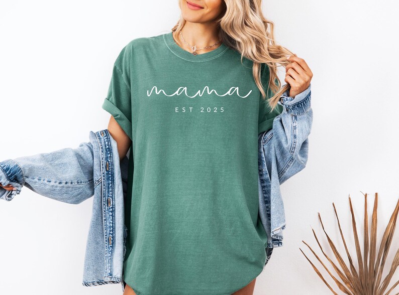 May include: A green t-shirt with the text "mama est 2023" in white lettering.