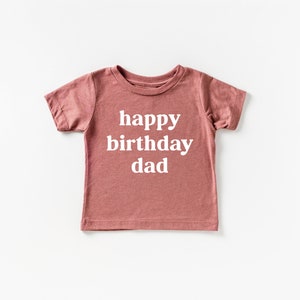 May include: A dusty rose short-sleeved t-shirt with the text "happy birthday dad" printed in white.