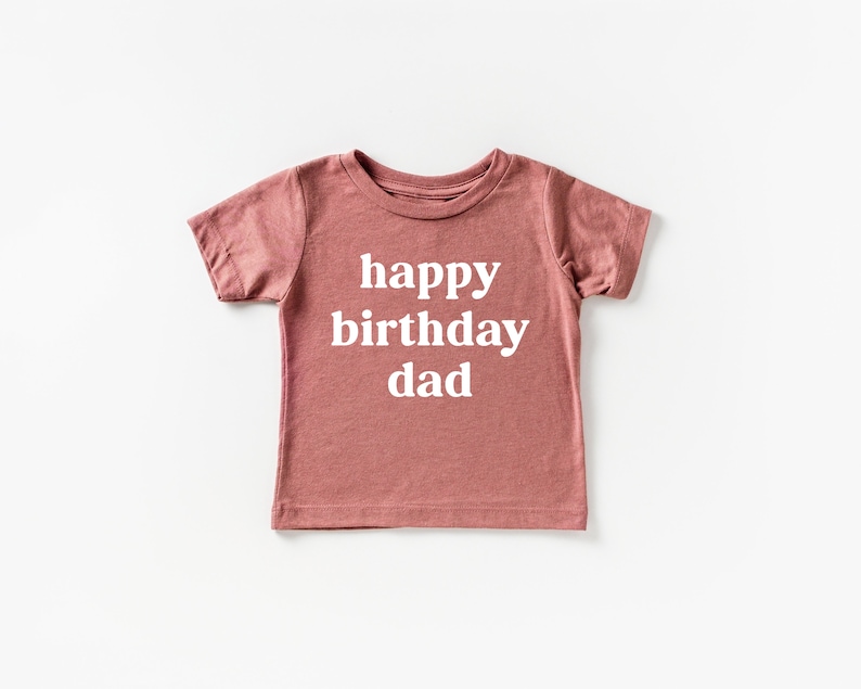 May include: A dusty rose short-sleeved t-shirt with the text "happy birthday dad" printed in white.