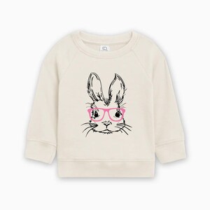 May include: A cream colored sweatshirt with a black and white illustration of a bunny wearing pink glasses.