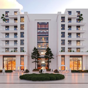 May include: A modern, multi-story building with a white facade, featuring multiple windows and balconies. The building has a symmetrical design with a central glass-enclosed section. Palm trees and landscaping are visible in the foreground, with a clear sky in the background.