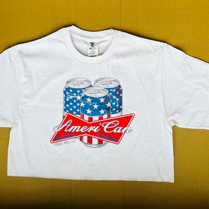 May include: White t-shirt with a graphic of four red, white, and blue cans with the text "Ameri Can" in red and white.