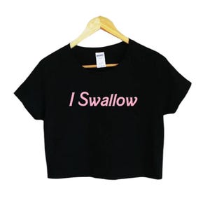 Puede incluir: Camiseta negra recortada con el texto "I Swallow" en letras rosas.