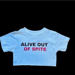 May include: White t-shirt with black text that reads "Alive Out Of Spite" in pink.