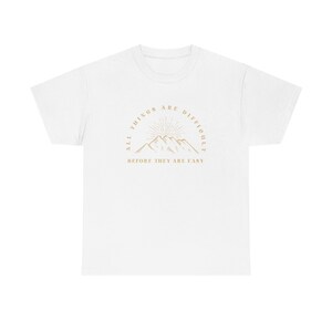 May include: White t-shirt with a graphic of mountains and the text "All things are difficult before they are easy."