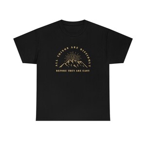 May include: Black t-shirt with a gold graphic of mountains and a sun with the text "All things are difficult before they are easy."