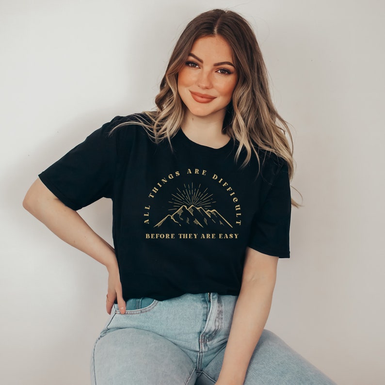 May include: A black t-shirt with a gold mountain graphic and the text "All things are difficult before they are easy".
