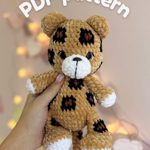 Op de afbeelding: Een gehaakt luipaard knuffeltje gemaakt van beige, bruin en wit garen met zwarte luipaardvlekken, donkere ogen en een witte snuit. De tekst "PDF pattern" staat in witte letters boven het knuffeltje, wat duidt op een digitaal instructiebestand.