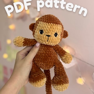 Peut inclure: Une peluche singe au crochet faite de fil doux marron et beige avec des yeux de sécurité noirs et un nez brodé. Le texte "PDF pattern" est affiché en lettres blanches en haut de l'image, indiquant qu'il s'agit d'un guide numérique.