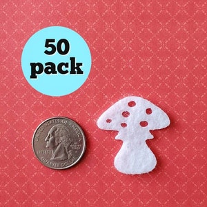 May include: A pack of 50 white felt mushroom shapes, each about the size of a US quarter. The mushrooms have a white stem and a white cap with a dotted pattern.