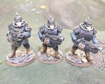 May include: Three painted miniature figures of soldiers wearing black and grey uniforms with helmets and holding guns. The figures are standing on round bases.