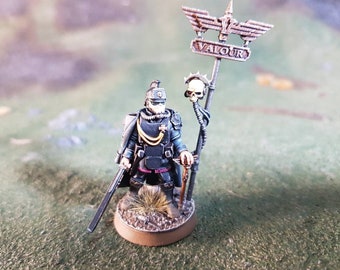 May include: A miniature figure of a soldier wearing a black uniform and a helmet with a skull on top. The soldier is holding a sword and a gun. The figure is standing on a base with a sign that says "VALOUR".