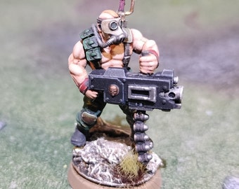 May include: A painted miniature figure of a soldier wearing a gas mask and holding a large machine gun. The figure is standing on a small, brown base.
