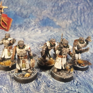 Może przedstawiać: Grupa sześciu pomalowanych miniaturek w kolorze białym, zielonym i brązowym, ubranych w białe płaszcze i trzymających broń. Figurki stoją na okrągłych podstawkach z czaszkami i innymi detalami.