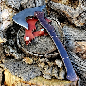 May include: A brown leather-wrapped axe with a dark brown wooden handle. The axe is resting on a tree stump with a brown leather sheath.