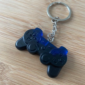 May include: A black and blue plastic video game controller keychain with a silver key ring and chain.
