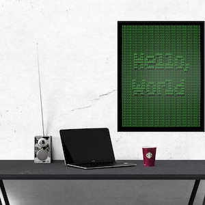 Könnte beinhalten: Ein schwarzer gerahmter Poster mit einem grünen Pixel-Design, auf dem "HELLO WORLD" steht, an einer weißen Wand. Ein Laptop, ein Vintage-Radio und eine rote Tasse stehen auf einem schwarzen Tisch vor dem Poster.