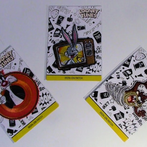 May include: Three iron-on patches featuring characters from Looney Tunes. The first patch shows Bugs Bunny peeking out of a television set. The second patch shows Sylvester the Cat chasing Tweety Bird. The third patch shows Taz the Tasmanian Devil in a whirlwind.