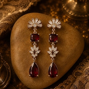 Peut inclure: Une paire de boucles d'oreilles pendantes dorées avec un sommet en éventail orné de pierres claires, une pierre rouge foncé carrée, un motif floral de pierres claires en marquise et une pierre rouge foncé en forme de goutte.