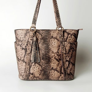 May include: A brown leather tote bag with a snakeskin pattern. The bag has a zip closure and a tassel on the front.