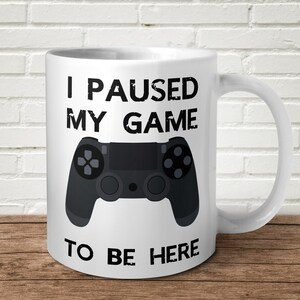May include: White ceramic mug with a black and white design. The mug features a video game controller and the text "I paused my game to be here".