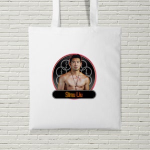 May include: White tote bag with a red and black circle design featuring a photo of Simu Liu. The circle has a gray design with the text "Simu Liu" in a red and black rectangle below the circle.