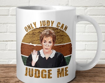 以下が含まれることがあります： ジャッジ・ジュディのグラフィックと「ONLY JUDY CAN JUDGE ME」の文字が入った白いセラミックマグ。デザインにはレトロな夕日の背景が含まれています。マグカップにはカーブしたハンドルが付いています。テキストは使い古されたフォントです。