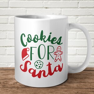 May include: White ceramic mug with the words "Cookies FOR Santa" in green and red script. The design includes a Santa hat, gingerbread man, and a cookie. The mug has a curved handle.
