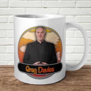 May include: White ceramic mug with a colorful graphic of a man with a black suit and the text "Greg Davies".