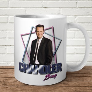 May include: White ceramic mug with a colourful geometric design featuring a portrait of Chandler Bing from the TV show Friends. The text "Chandler Bing" is printed in a bold, black font.