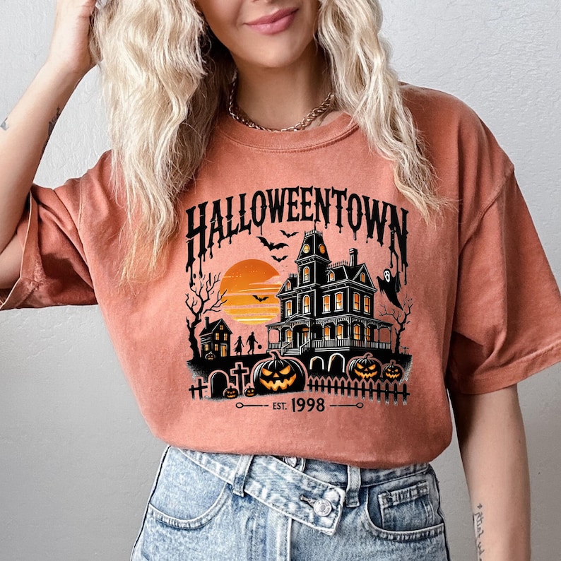 May include: A burnt orange t-shirt with a graphic print of a spooky house, a sunset, and the text "HALLOWEENTOWN EST. 1998".