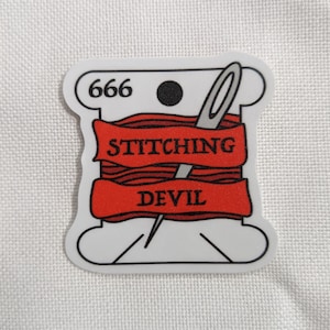 May include: A white sticker in the shape of a thread spool with a red banner that reads "STITCHING DEVIL". A needle is threaded through the red thread. The number "666" is printed at the top.
