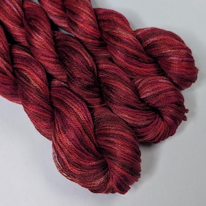 May include: Close-up of a skein of deep red embroidery floss with white and pink highlights.
