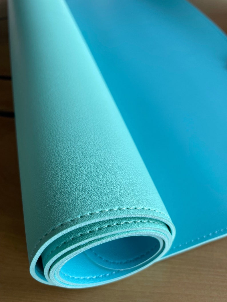 Pu&ograve; includere: Un tappetino da scrivania turchese arrotolato, con una superficie strutturata. Il tappetino &egrave; realizzato in materiale flessibile e presenta un bordo cucito. Il colore passa da un turchese pi&ugrave; chiaro a un blu pi&ugrave; brillante.