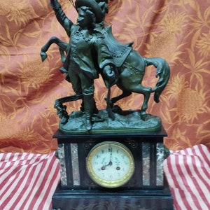 Può includere: Un orologio in marmo nero con una scultura in bronzo di un uomo a cavallo. Il quadrante dell'orologio ha numeri romani e una cornice dorata.