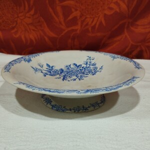 Peut inclure: Un bol en céramique blanche sur un piédestal avec un motif floral bleu. Le bol a un bord festonné et une base surélevée.