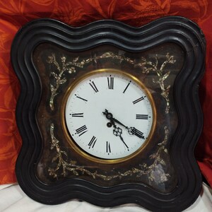 May include: A black wooden clock with a white face and Roman numeral markings. The clock is decorated with a mother-of-pearl inlay design.