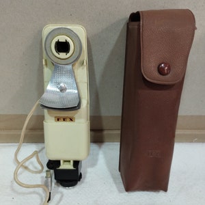 May include: A white and brown vintage FEX flash unit with a cord and a brown leather case.