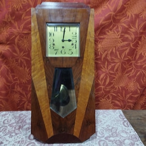 May include: A vintage wooden clock with a gold face and black hands. The clock has a geometric design with a mirrored pendulum.