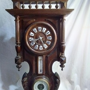 Puede incluir: Un reloj de pared antiguo de madera marrón oscuro, con una esfera redonda con números romanos. Debajo de la esfera hay un termómetro y un barómetro. El reloj tiene tallas decorativas.