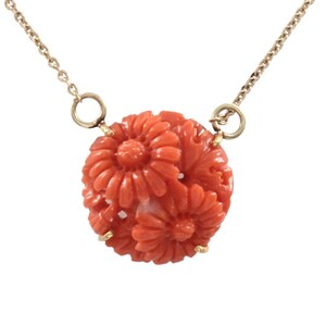 Pu&ograve; includere: Una delicata collana a catena d'oro con un ciondolo rotondo in corallo con un design floreale intagliato.