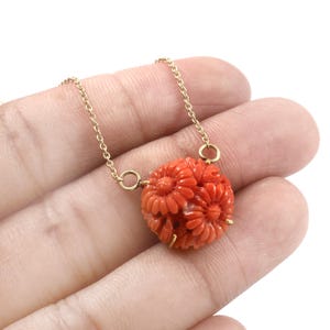 Pu&ograve; includere: Una delicata collana a catena d'oro con un ciondolo in corallo intagliato. Il ciondolo &egrave; una sfera rotonda con un motivo floreale. Il corallo &egrave; di un colore rosso-arancio vibrante.