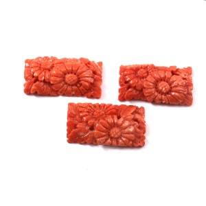 May include: Three carved coral flower beads in a rectangular shape. The beads are a vibrant orange-red colour and feature intricate floral designs.