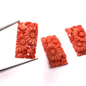 May include: Three carved coral pieces with a floral design. The coral is a vibrant orange-red colour.