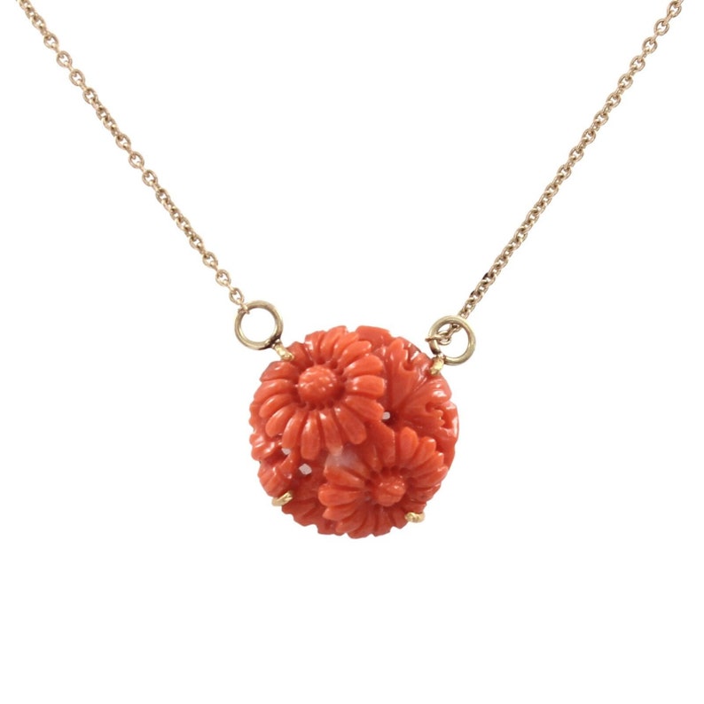Pu&ograve; includere: Una delicata collana a catena d'oro con un ciondolo rotondo in corallo con un design floreale intagliato.